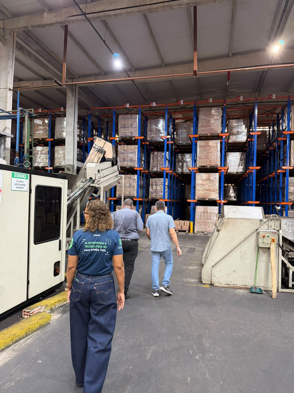 Equipe da Atlante caminhando pelo corredor de um centro de distribuição, entre porta-paletes carregados e equipamentos de movimentação